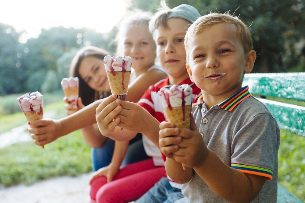 Group of four happy children eating ice cream together outdoor.