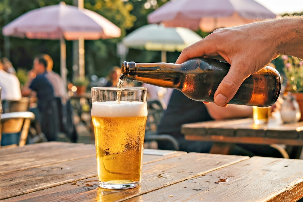Man pouring cold beer into glass at outdoor cafe.